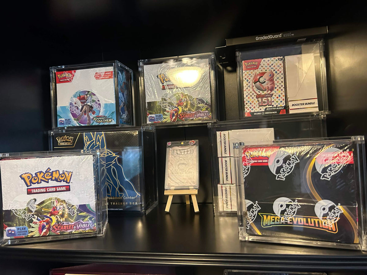 Sealed Pokémon boxes on a dark shelf in TCG Protectors acrylic cases